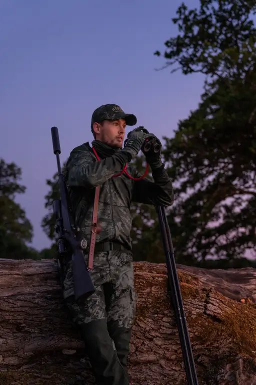 Mann mit Tarnbekleidung auf Jagd in der Dämmerung mit Fernglas