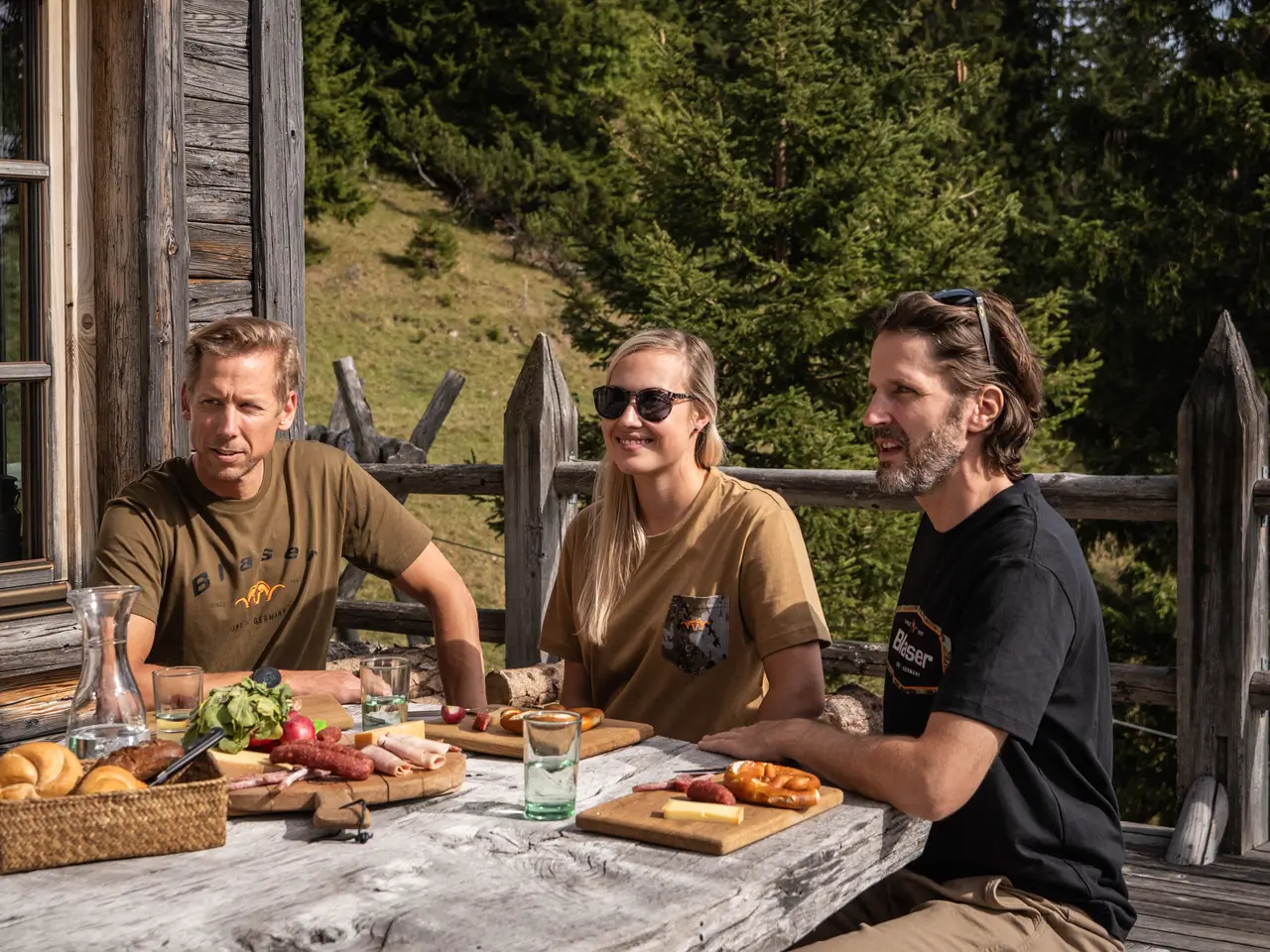 Zwei Herren und eine Damen sitzen am gedeckten Tisch und tragen Blaser-Shirts